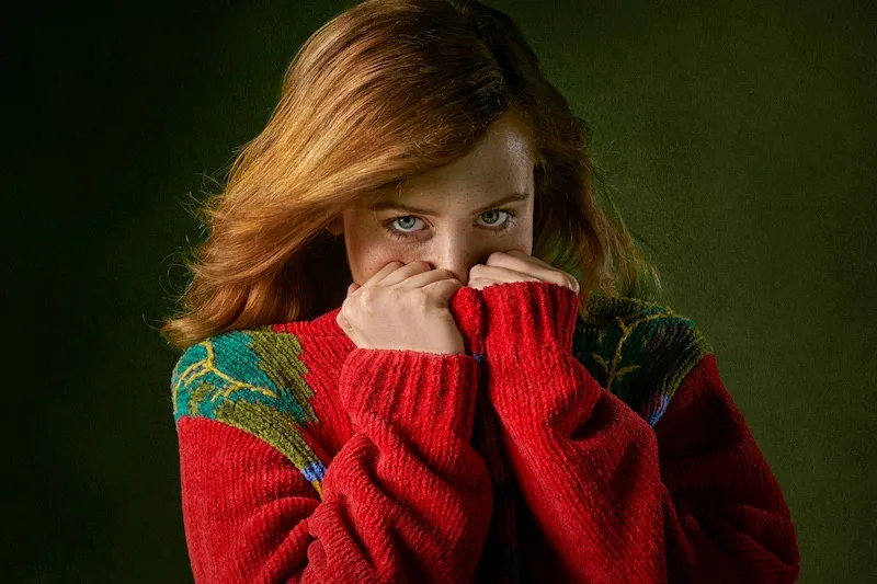 Young woman in an oversized red sweater covering part of her face, expressing vulnerability, anxiety, and emotional growth.