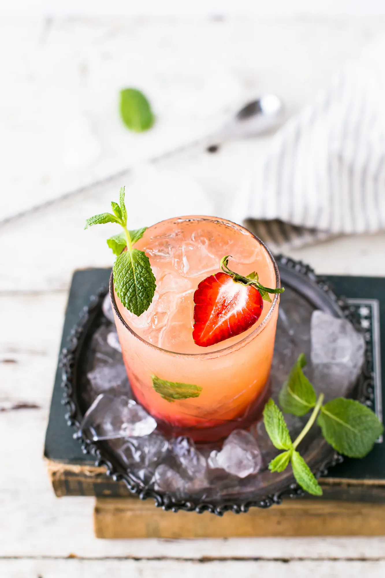 Pink iced drink garnished with strawberry and mint on a tray of ice, representing celebration and refreshment after graduation.