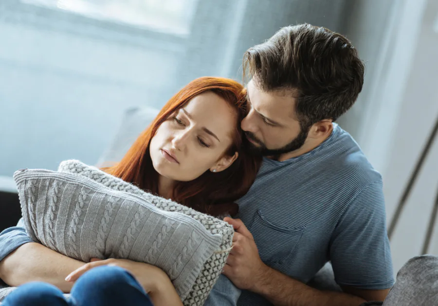 Pasangan duduk rapat di atas sofa, dengan seorang kelihatan sedih sementara seorang lagi cuba menenangkan
