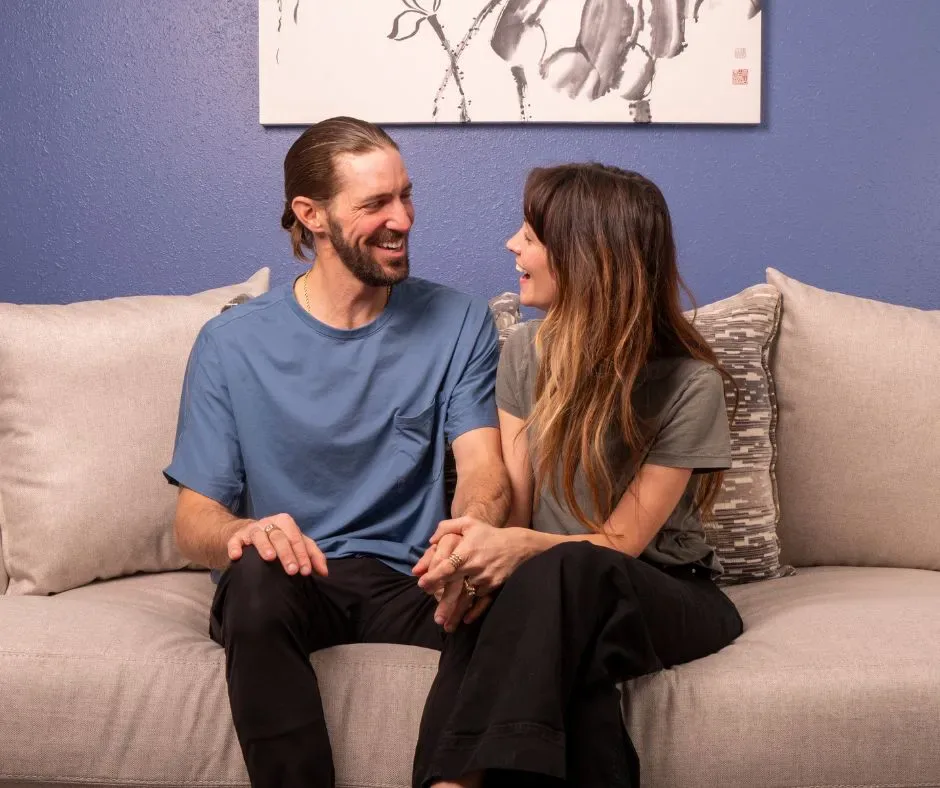 Couple sitting on a sofa smiling at each other and holding hands, showing emotional connection in marriage.