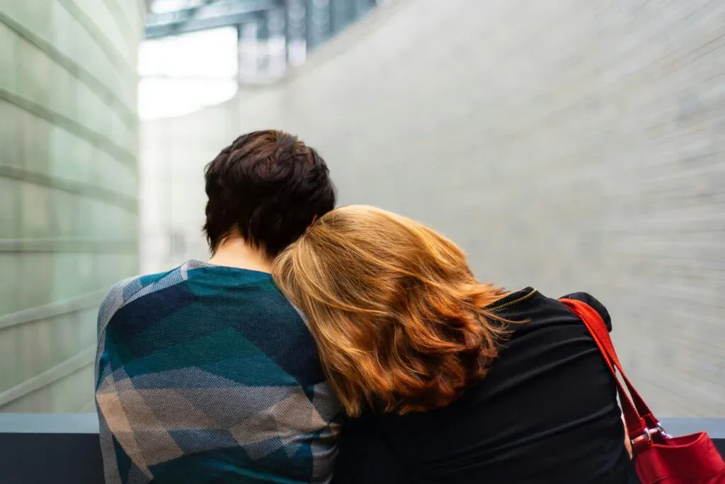 Two people sitting closely with one leaning on the other's shoulder, symbolizing emotional support behind graduation success.
