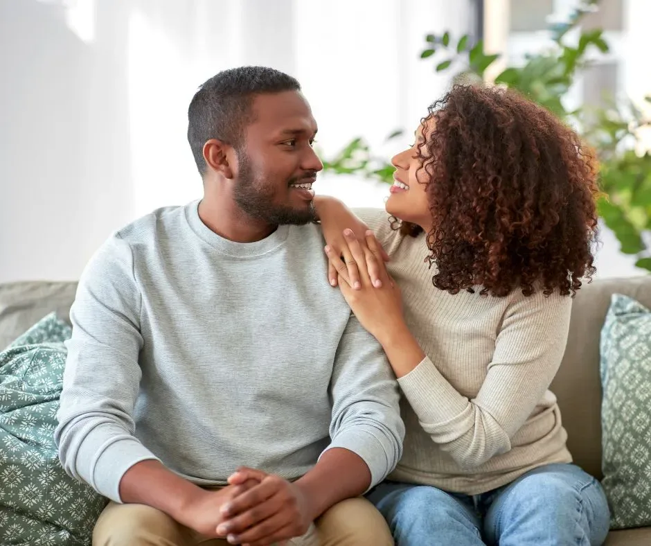Happy couple sitting on a couch making eye contact, showing affection, emotional safety, and healthy communication before marriage
