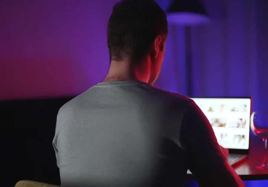 Hombre sentado solo frente a un ordenador en una habitación oscura iluminada con luz morada y azul, representando el aislamiento digital en las relaciones